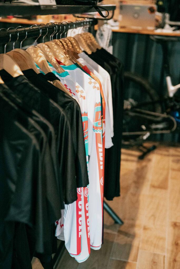 Row of colorful sports jerseys on wooden hangers in a clothing store, with black garments nearby.