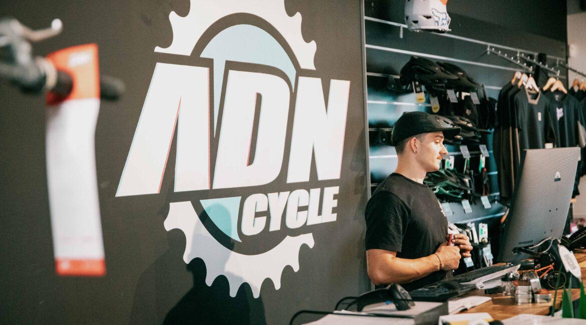 Motorcycle shop counter with staff member in a black cap, wall logo featuring a gear, and helmets on display.