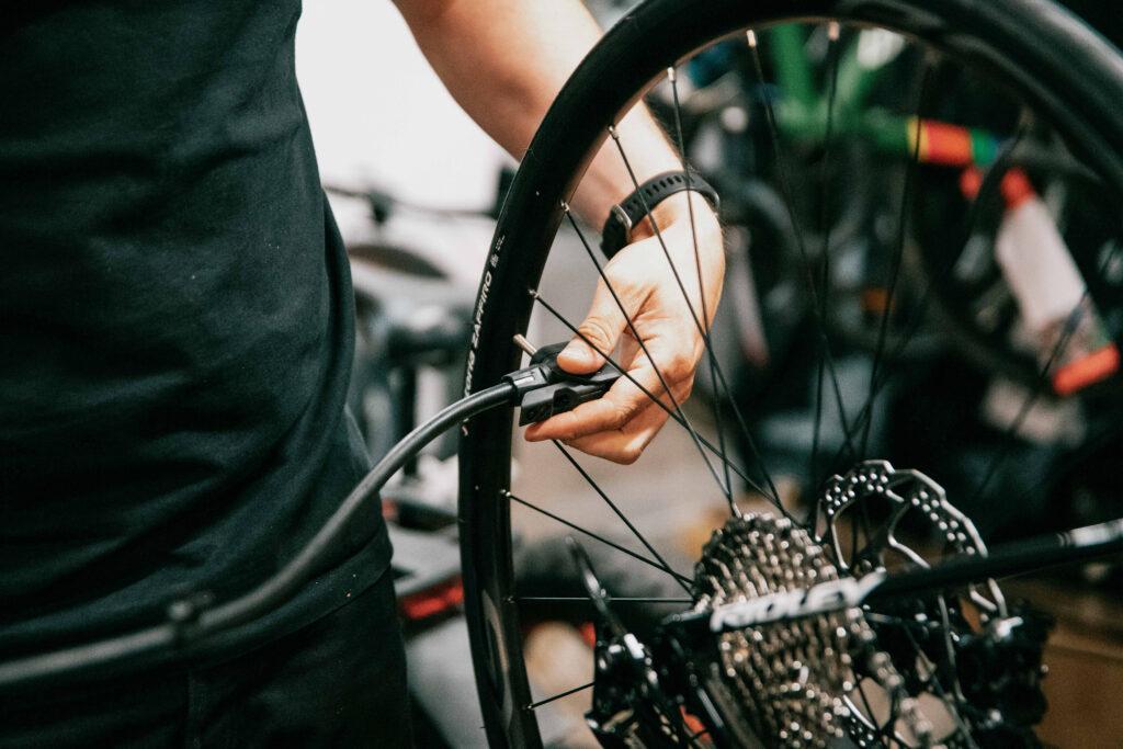 Close-up of a person in a black shirt working on a bicycle wheel, hand tightening or adjusting the wheel in a workshop.