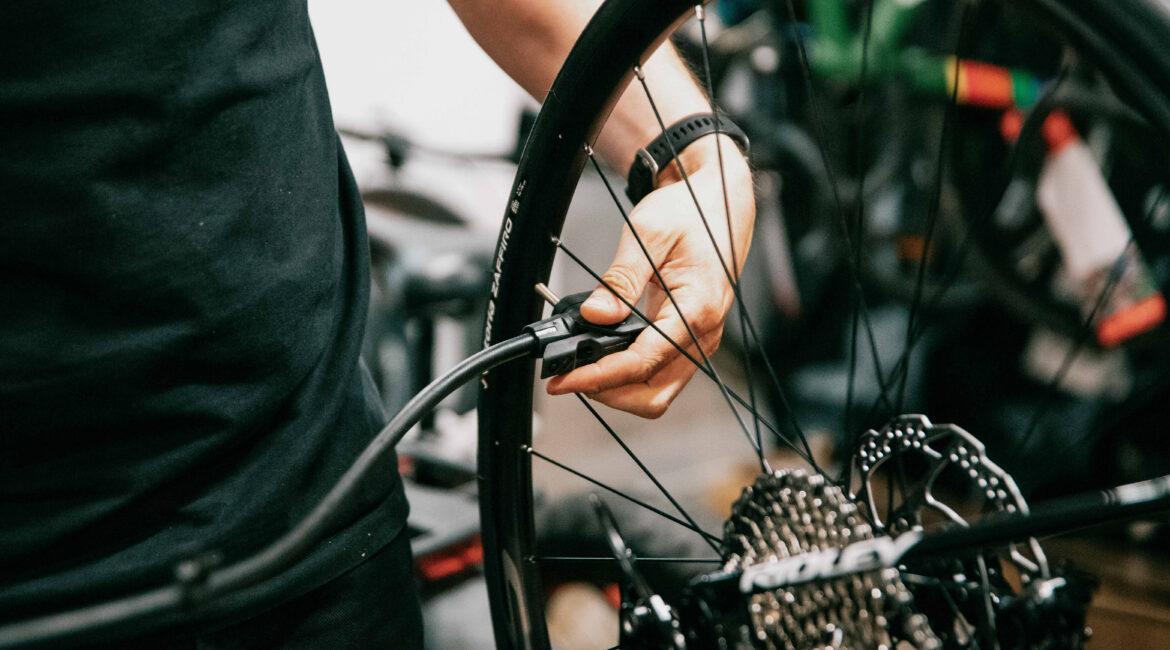 Close-up of a person in a black shirt working on a bicycle wheel, hand tightening or adjusting the wheel in a workshop.