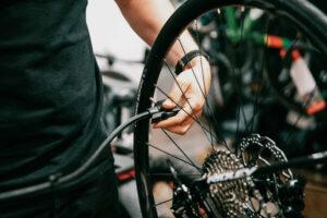 Close-up of a person in a black shirt working on a bicycle wheel, hand tightening or adjusting the wheel in a workshop.