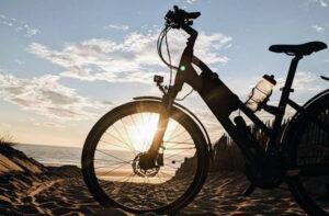 Electric bike on a sandy beach at sunset, the sun low behind the front wheel creating a silhouette.